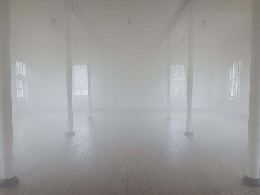 "At or near the surface of the earth" by Sholeh Asgary An art installation at Headlands Center for the Arts features a foggy room with a wood floor, four windows, and six columns.
