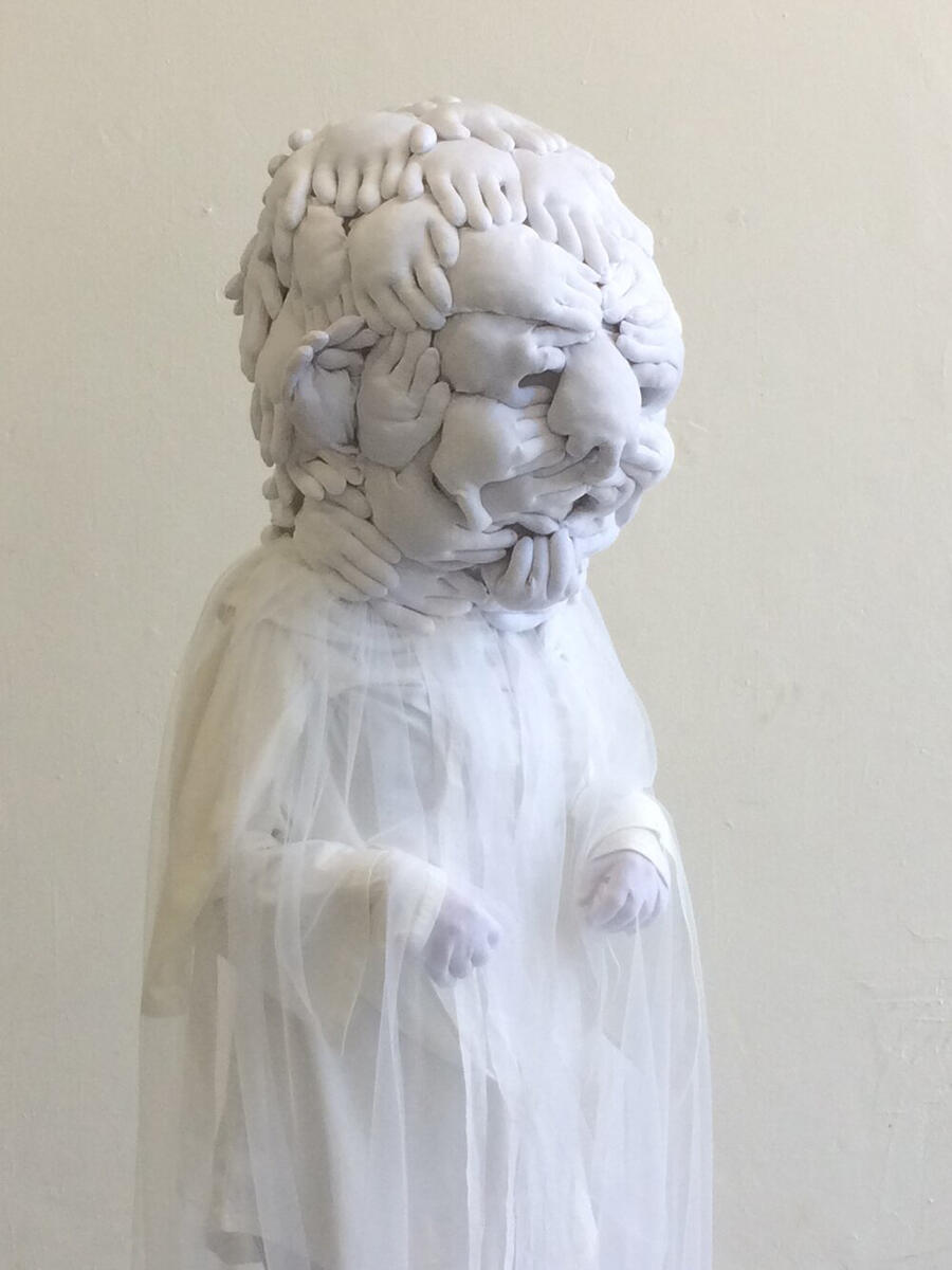 A sculpture of a humanlike figure with a head made of several interlocking hands.