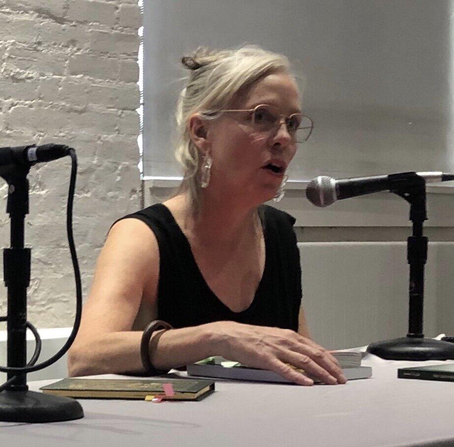 Professor Anne Walsh Female-presenting person with white hair and black v-neck top speaks into a microphone, viewed from the chest up.